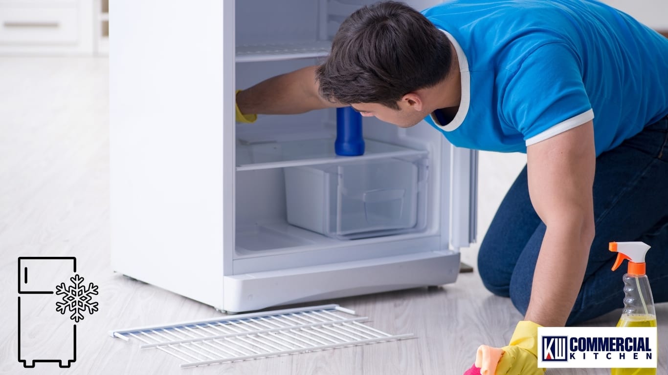 Technician cleaning the interior shelves of a commercial fridge—routine maintenance and airflow keep cabinets efficient and able to hold ≤5 °C.