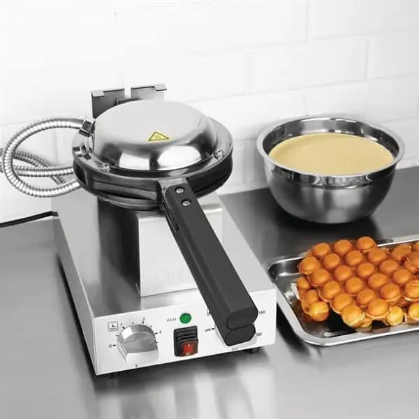 Bubble waffle maker on stainless bench with batter bowl and finished egg waffle